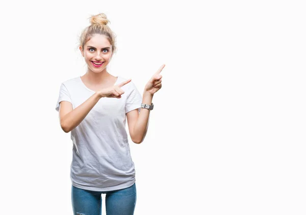 年轻美丽的金发碧眼的女人穿着白色的 T恤在孤立的背景微笑着 看着相机指向用两只手和手指指着一边 — 图库照片