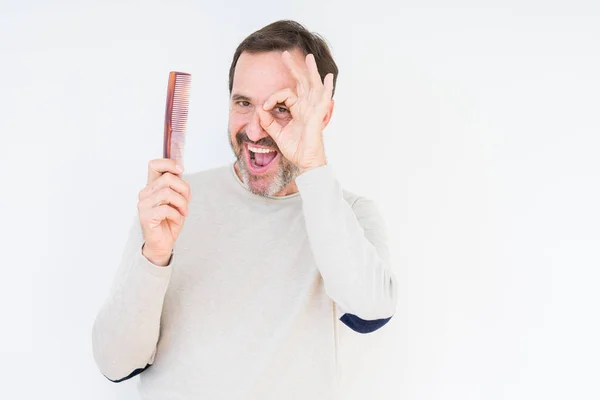 Senior man holding hair comb over isolated background with happy face smiling doing ok sign with hand on eye looking through fingers