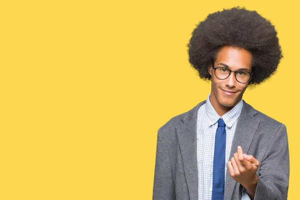 Young african american business man with afro hair wearing glasses Beckoning come here gesture with hand inviting happy and smiling
