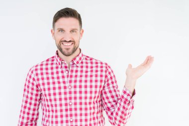 Neşeli sunulması ve kameraya bakarak avucunun ile işaret gülümseyen izole arka plan üzerinde gömlek giymiş genç yakışıklı adam.