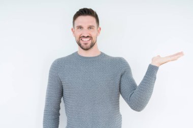 Neşeli sunulması ve kameraya bakarak avucunun ile işaret gülümseyen izole arka plan üzerinde rahat kazak giyen genç yakışıklı adam.
