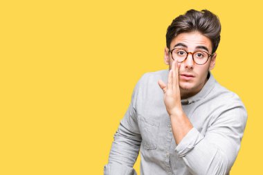 Genç yakışıklı adam gözlük izole arka plan üzerinde kötü amaçlı konuşma konuşma fısıldayan gizli söylenti söylüyor dudaklarından el