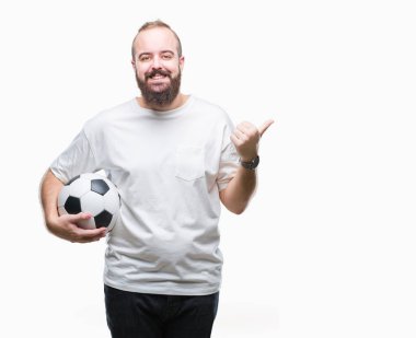 İşaret ve başparmak kadar mutlu yüz gülümseyen tarafı ile gösteren izole arka plan üzerinde futbol futbol topu tutan genç beyaz hipster adam