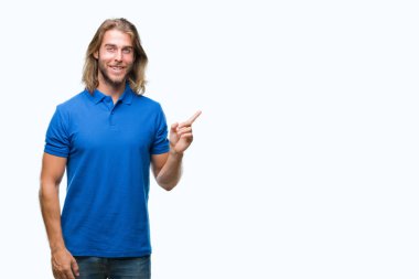 Kameraya bakarak yan el ve parmak ile işaret eden genç yakışıklı adam yüzünde kocaman bir gülümseme ile izole arka plan üzerinde uzun saçlı.