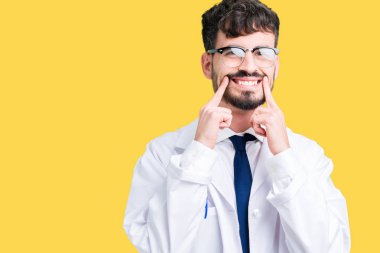 Beyaz önlük üzerinde izole giyen genç profesyonel bilim adam arka plan gülen açık ağız ile parmak işaret ve neşeli zorlama gülümseme