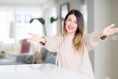 Evde kış kazak giyen genç güzel kadın sarılmak için kollarını açarak gülümseyen kamera bakıyor. Neşeli ifade kucaklayan mutluluk.