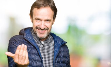 Orta yaş yakışıklı adam giyen kış ceket Beckoning gel burada mutlu ve gülümseyerek el davet ile jest