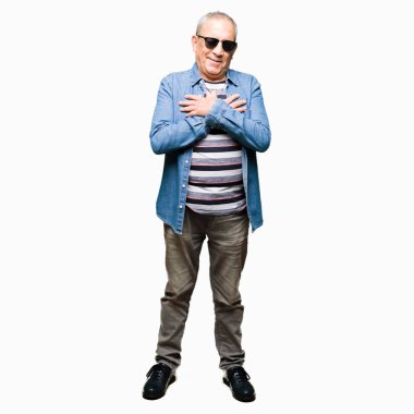 Denim ceket ve ile gülümseyen güneş gözlüğü takan yakışıklı komuta sizde kapalı gözler ve yüzünde minnettar jest ile göğüs üzerinde eller. Sağlık kavramı.