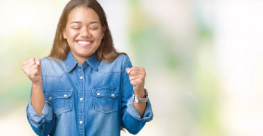 Zafer kutluyor gülümseyen izole arka kolları olan başarı için heyecan üzerinde mavi kot gömlek giyen genç güzel esmer kadın kaldırdı. Kazanan kavramı.