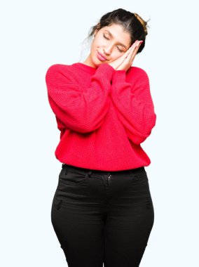 Rüya ve elleri ile kapalı gözler gülümseyen birlikte poz kırmızı kazak ve topuz uyku giyen genç güzel kadın yorgun.