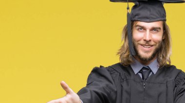 Genç yakışıklı adam uzun saçlı sarılmak için kollarını açarak gülümseyerek kameraya bakarak izole arka plan üzerinde mezun oldu. Neşeli ifade kucaklayan mutluluk.