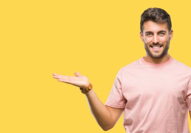 Genç yakışıklı adam neşeli sunulması ve kameraya bakarak avucunun ile işaret gülümseyen izole arka plan üzerinde.