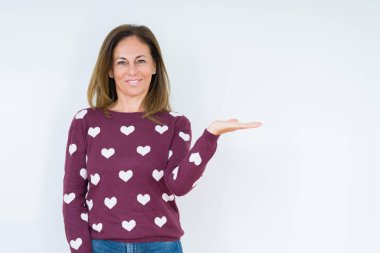 Neşeli sunulması ve kameraya bakarak avucunun ile işaret gülümseyen izole arka plan üzerinde kalp kazak giyen güzel orta yaş kadın.