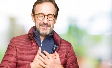 Orta yaş yakışıklı adam gözlük ve ile gülümseyen kış ceket giyen kapalı gözler ve yüzünde minnettar jest ile göğüs üzerinde eller. Sağlık kavramı.