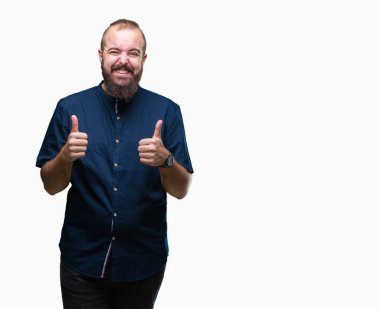 Genç beyaz hipster adam izole arka plan başarı işareti başparmak gülümseyen ve mutlu el ile olumlu hareketi yapıyor. Neşeli bir ifadeyle, kazanan jest kameraya bakıyor.