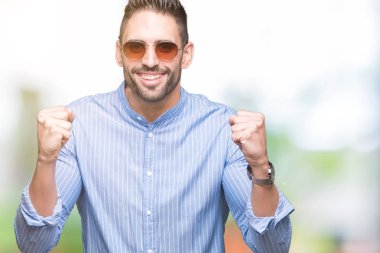 Yakışıklı delikanlı izole arka plan kutlama üzerinde güneş gözlüğü takıyor şaşırttı ve başarı için kaldırdı kollarını açarak hayret ve gözleri açık. Kazanan kavramı.