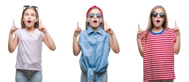 Kolaj izole arka plan üzerinde güneş gözlüğü takmış genç küçük kız çocuk hayret ve yukarıya bakıyor ve parmakları ile işaret ve silah kaldırdı şaşırttı.