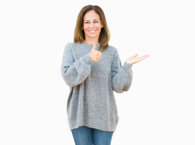 Üzerinde kış kazak giyen güzel orta yaş kadın arka plan gösteren palm el ve iş tamam jestle başparmak yukarıya, mutlu ve neşeli gülümseyen izole