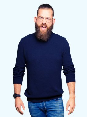 Şüpheci ve alaycı, şok karşısında, gözlük ve balıkçı yaka kazak giyen genç sarışın adam açık ağız ile şaşırttı