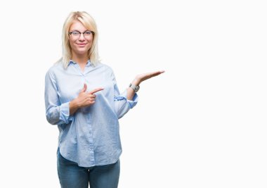 Hayret ve el ile sunulması ve parmak ile işaret ederken kameraya gülümseyen izole arka plan üzerinde gözlük takan genç güzel sarışın iş kadını.