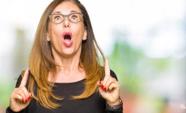 Gözlüklü güzel orta yaş kadın hayrete ve yukarıya bakıyor ve parmakları ile işaret ve silah kaldırdı şaşırttı.