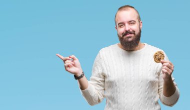 Genç hipster man izole arka tarafına el ve parmak ile işaret çok mutlu üzerinde çikolata çerez yemek