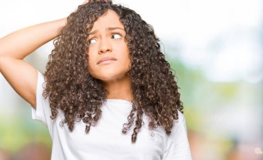 Kıvırcık saçlı beyaz t-shirt giyen genç güzel kadın yanıltır ve soru hakkında merak ediyorum. Şüphe, kafasına el ile düşünme ile belirsiz. Dalgın kavramı.