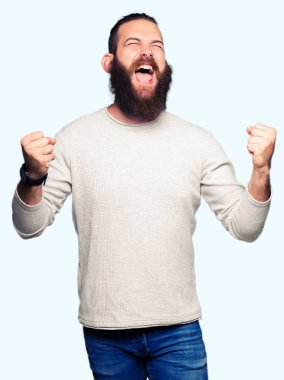 Gülümseyen ve başarı için çığlık rahat kazak çok mutlu ve heyecanlı kaldırdı, silah ile kazanan jest yapıyor giyen genç sarışın adam. Kutlama kavramı.