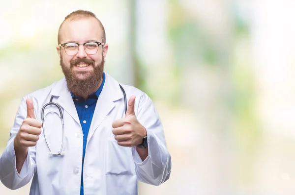 肯定的なジェスチャーをして承認する孤立した背景に医療白衣を着た若い白人医師男は親指を笑顔と幸せな成功のためです カメラ 勝者のジェスチャーを見てください — ストック写真