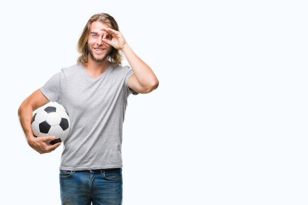 Young handsome man with long hair over isolated background holding football ball with happy face smiling doing ok sign with hand on eye looking through fingers