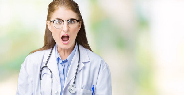 Взрослая женщина-врач средних лет в медицинском халате на изолированном фоне, напуганная и потрясенная удивлением выражением лица, страха и возбужденного лица
.