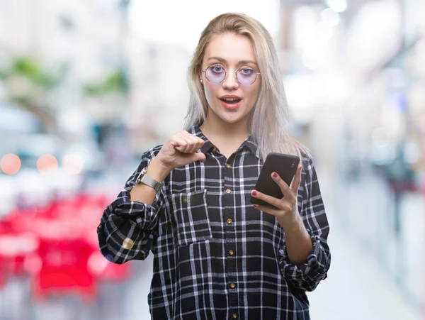 若いブロンドの女性テキスト メッセージを自分自身に驚き顔人差し指と孤立の背景にスマート フォンを使用してメッセージを送信します — ストック写真