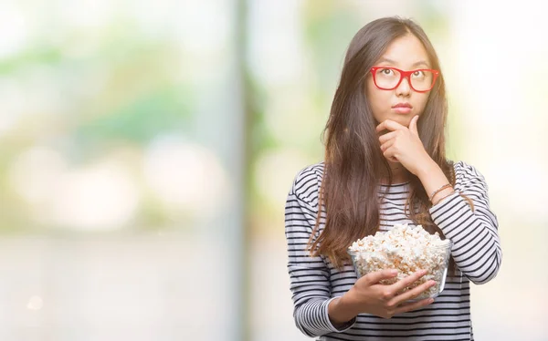 若いアジア女性に関する質問は 非常に混乱して考え分離背景深刻な顔を考えての上でポップコーンを食べて — ストック写真