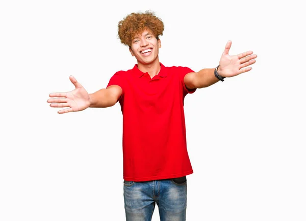 年轻英俊的男子与非洲头发红色 T恤看着镜头微笑着张开双臂拥抱 拥抱幸福的快乐表情 — 图库照片