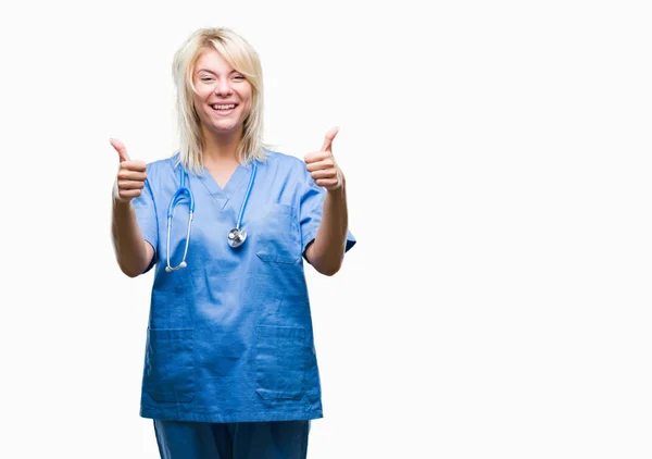 年轻美丽的金发碧眼的医生妇女穿着医疗制服在孤立的背景成功标志做积极的手势 竖起大拇指微笑和快乐 带着欢快的表情 获胜者的手势看着镜头 — 图库照片