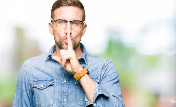 Handsome man wearing glasses asking to be quiet with finger on lips. Silence and secret concept.