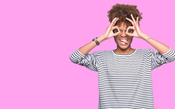 美丽的年轻非洲裔美国妇女戴眼镜在孤立的背景做确定的手势像双筒望远镜伸出舌头 眼睛通过手指看 疯狂的表达 — 图库照片