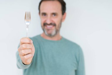 Komuta sizde ayakta ve diş gösterilen kendine güvenen bir gülümsemeyle gülümseyerek mutlu bir yüz ile izole arka plan üzerinde gümüş çatal tutan