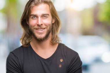 Kameraya bakarak çapraz silah ile gülümseyen izole arka plan mutlu yüzüne uzun saçlı Genç yakışıklı adam. Olumlu bir kişi.