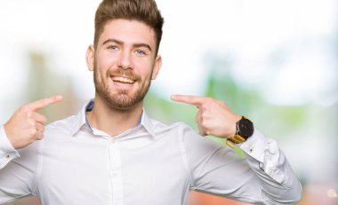 Kendinden emin gösterilen ve işaret parmakları diş ve ağız ile gülümseyen genç yakışıklı iş adamı. Sağlık kavramı.