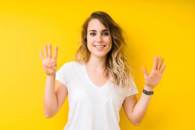 Young beautiful blonde woman over yellow background showing and pointing up with fingers number nine while smiling confident and happy.