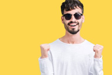 Yakışıklı delikanlı izole arka plan kutlama üzerinde güneş gözlüğü takıyor şaşırttı ve başarı için kaldırdı kollarını açarak hayret ve gözleri açık. Kazanan kavramı.