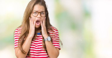 Giyen genç güzel esmer kadın gözlük ve t-shirt korkuyor ve şok sürpriz ifade, korku ve heyecan yüz ile izole arka plan üzerinde çizgili.