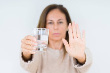 Orta yaş kadın bardak su içme arka plan açık eliyle dur işareti ile ciddi ve kendine güvenen ifade, savunma jest yapıyor izole