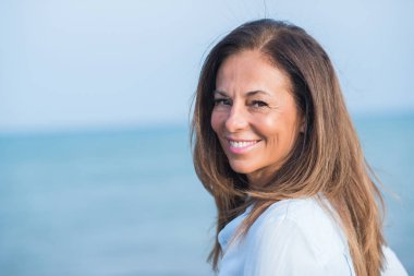 Okyanus, yüzünde gülümseme ile duran güzel orta yaş İspanyol kadın. Kendinden emin ve neşeli gülümseyen güneşli bir deniz manzaralı.