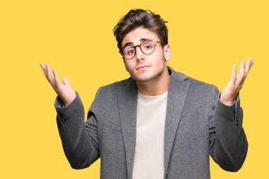 Üzerinde gözlük takan genç iş adamı arka plan clueless ve şaşkın bir ifadeyle kollar ve eller kaldırdı izole. Şüphe kavramı.