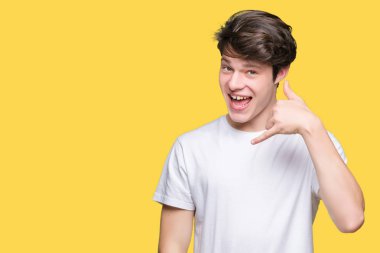 Genç yakışıklı adam giyiyor rahat beyaz tişört yapıyor gülümseyen izole arka plan üzerinde telefon hareketi ile el ve parmak telefonda konuşuyor gibi. Kavramları iletişim.