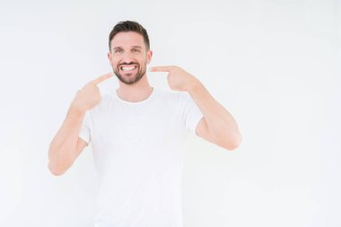 Kendinden emin gösterilen ve işaret parmakları diş ve ağız ile gülümseyen izole arka plan üzerinde rahat beyaz t-shirt giyen genç yakışıklı adam. Sağlık kavramı.