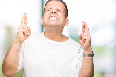 Orta yaş Arap adam wearig geçiş parmakları umut ve gözler gülümseyen izole arka plan üzerinde beyaz t-shirt kapalı. Şans ve batıl kavramı.