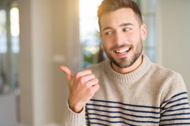 Evde genç yakışıklı adam işaret ve mutlu yüzü gülümseyerek yan başparmak ile gösteren